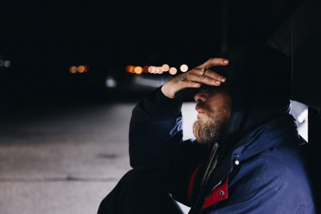 Bearded homeless man holding his head